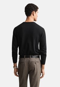 Čierny pulóver s dlhým rukávom a okrúhlym výstrihom, kombinovaný s hnedými nohavicami s vzorom jelenieho zuba. Pulóver má textúrované rukávy a priliehavý strih.