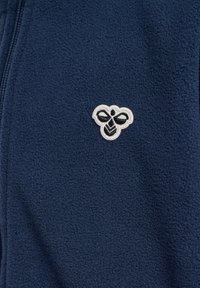 Marinblå fleecejacka med mjuk textur, med en vit broderad bi-logotyp på övre vänstra sidan. Helzip-design utan ytterligare detaljer.