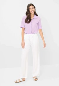 Lila korte mouw button-up shirt met kraag, gecombineerd met witte, losse broek en witte sandalen. Soepele stof en relaxte pasvorm.