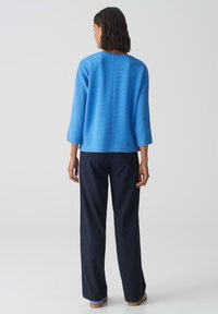 Blauwe geribbelde trui met een relaxte pasvorm en driekwartmouwen, gecombineerd met losse marineblauwe broek en blauwe accenten aan de zoom.