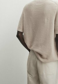 Light beige knitted short-sleeve top with a loose fit, featuring a textured pattern and a round neckline, paired with cream-colored trousers.