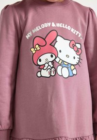 Lila långärmad sweatshirt med grafiker av My Melody och Hello Kitty, rundad halsringning och gatherad nederkant. Mjukt, lätt tyg.