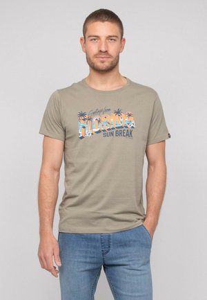 T-shirt vert olive en coton doux, avec une impression graphique "Salutations de Floride" et des accents de palmier sur le devant.