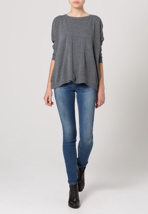 Grauer übergroßer Pullover mit rundem Ausschnitt, geripptem Saum und lockeren Ärmeln, kombiniert mit eng anliegenden blauen Jeans und schwarzen Stiefeletten.