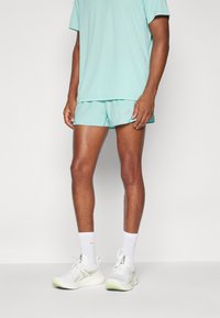 Mint green athletic shorts and matching t-shirt, made of lightweight fabric. White sneakers with green accents and visible laces.