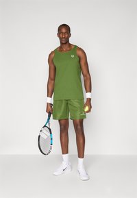 Camisola atlética verde de alças e calções feitos de tecido macio. A camisola tem um decote redondo e um logótipo; os calções apresentam um cós elástico e bolsos.