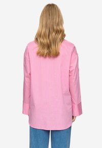 Lange mouwen shirt in lichtroze met verticale witte strepen. Zachte stof, losse pasvorm, afgeronde zoom en licht oversized mouwen.