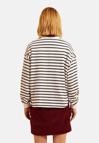Sudadera a rayas en color crema y marino, con un corte holgado y hombros caídos, combinada con una falda de pana burdeos.