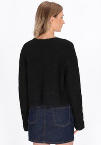 Maglione nero a maglia con design cropped e maniche ampie, abbinato a una gonna in denim blu con tasche posteriori e cuciture visibili.