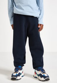 Pantaloni della tuta in pile blu navy con una vestibilità rilassata, abbinati a sneakers colorate con dettagli bianchi, blu navy e accenti rossi e verdi.