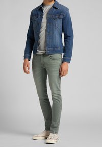 Džínová bunda v tmavě modré, šedé tričko, světle zelené slim-fit džíny a béžové tenisky s červenými akcenty. Neformální outfit s klasickým designem.