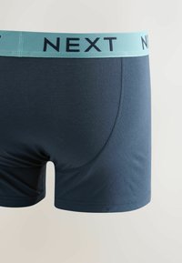 Boxer homme bleu marine avec ceinture élastique bleu clair portant le logo de la marque "NEXT" en texte noir.