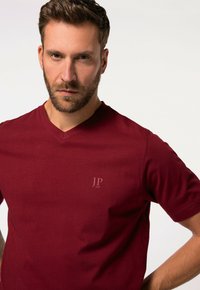 Camiseta de algodón burdeos con corte en V y mangas cortas, que presenta un sutil logo "JP 1880" en el pecho. Textura suave, ajuste casual.