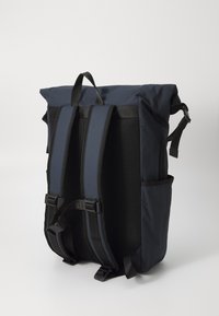 Ryggsekk i mørk marineblått stoff, med rulltoppsdesign, polstrede stropper, nettingryggpanel og justerbare sidelommer.