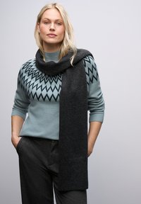 Jasnoniebieski sweter z czarnym wzorem w zygzak, zestawiony z ciemnoszarym szalikiem. Materiały wydają się miękkie z teksturowanym wykończeniem.
