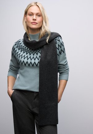 Jasnoniebieski sweter z czarnym wzorem w zygzak, zestawiony z ciemnoszarym szalikiem. Materiały wydają się miękkie z teksturowanym wykończeniem.