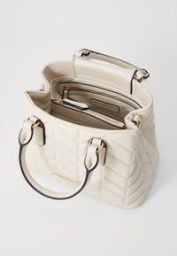 Geverfde crèmekleurige leren handtas met twee bovenhandvatten, gouden accenten en een zwarte rand. Het interieur bevat meerdere compartimenten en ritsen.