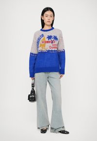 Kelių spalvų megztinis su mėlyna apatine dalimi, minkšta tekstūra, su grafiniu piešiniu, vaizduojančiu salas, burlaivį ir tekstą. Derinamas su šviesiais džinsais.