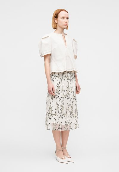 Λευκό βαμβακερό τοπ με φουσκωτά μανίκια, συνδυασμένο με φλοράλ πλισέ φούστα σε ανοιχτές αποχρώσεις και λευκά παπούτσια με τακούνι block και λεπτομέρεια με λουράκι.