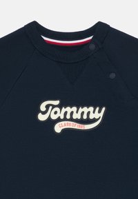Jūras spēku džemperis ar ribotu apkakli un raglanu piedurknēm. Iekļauj baltu izšūtu "Tommy" logotipu un "CLASS OF 1985" sarkanā krāsā.