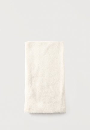 Un échantillon plié de tissu tricoté de couleur crème repose sur une surface gris clair.