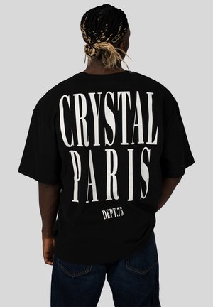 Černé oversized tričko s velkým bílým nápisem na zádech, který zní "CRYSTAL PARIS" a "DEPT.75", s kulatým výstřihem a krátkými rukávy.