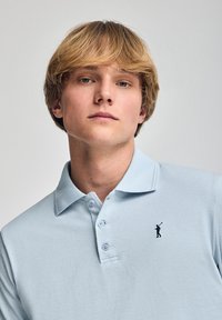 Polo de color azul claro en una mezcla de algodón, con una tapeta de tres botones y un pequeño logo bordado en el lado izquierdo del pecho.