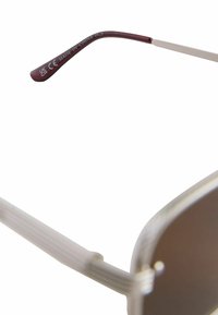 Sunglasses med runda grå linser, metallram och burgundy glasöron. Glasöronen har en gravyr: "CE MADE IN CHINA FC3." Slät yta.