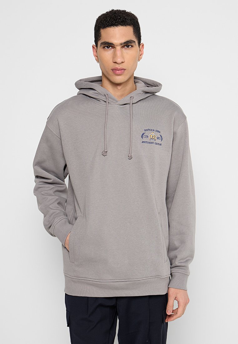 Lichtgrijze hoodie gemaakt van zachte stof. Beschikt over een voorzak, trekkoordkap en geborduurd logo op de linkerborst.