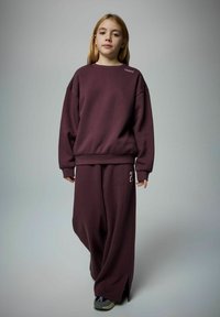 Vinröd oversized sweatshirt med rund hals och sidodetaljer, kombinerad med vida matchande byxor som har en nummerdetalj på sidan.