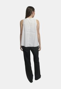 Top bianco senza maniche con dettaglio a chiave sulla schiena, abbinato a jeans neri a gamba larga. Tessuto liscio e silhouette rilassata e pettinata.