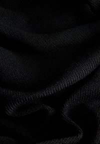 Tissu noir texturé avec de petits motifs tricotés visibles formant des plis et des courbes douces sous un faible éclairage.