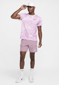 Roze gestippeld shirt met korte mouwen en bijpassende shorts, beide met het Nike-logo. Witte baseballcap en witte schoenen met zwarte accenten.