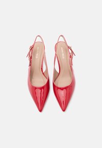 Κόκκινα πέδιλα από λουστρίνι με μυτερό μύτο, λουράκι στον αστράγαλο και αγκράφα σε χρυσή απόχρωση. Το εσωτερικό διαθέτει ουδέτερο επένδυση.