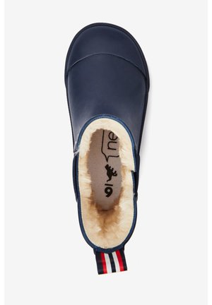 Chausson bleu marine à enfiler avec doublure en fourrure crème et languette de talon rayée rouge, blanche et bleue, vu de dessus.