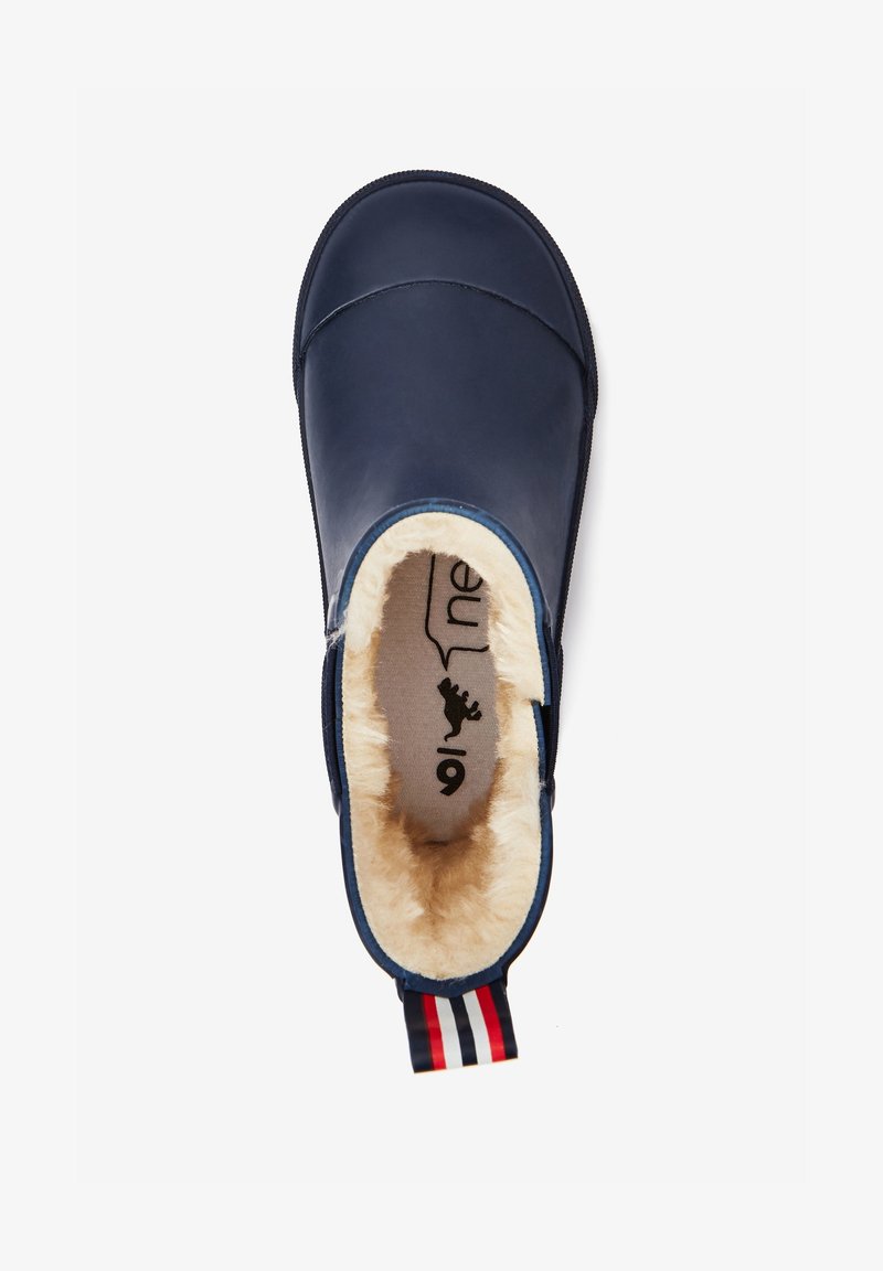Chausson bleu marine à enfiler avec doublure en fourrure crème et languette de talon rayée rouge, blanche et bleue, vu de dessus.