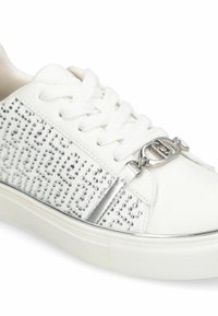 Baskets blanches avec un motif clouté sur le côté, des accents métalliques, des lacets blancs et une semelle en caoutchouc texturée.