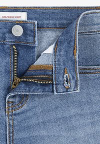 Σορτς από ανοιχτό μπλε τζιν με χρυστά ραφές και μεταλλικό φε ρμουάρ. Διαθέτει ετικέτα στη μέση με την επιγραφή "GIRLFRIEND SHORT" και μία μικρή θηλιά για ζώνη.