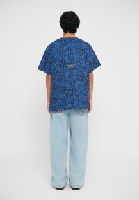 Zila leopardu raksta T-kreklā ar brīvu piegriezumu, ar apaļu kakla izgriezumu un īsām piedurknēm. Apvienots ar platām gaišām džinsām.