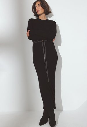 Black ribbed midi dress with a fitted silhouette, side zip detail, and black belt. Worn with pointed black ankle boots.