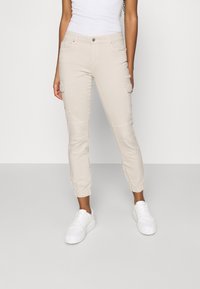 Beige cargo kalhoty s elastickými manžetami, několika kapsami a hladkým povrchem. Kombinované s bílými teniskami.