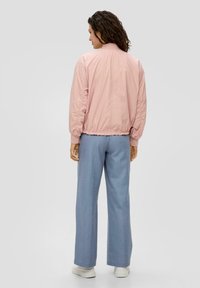 Veste bomber rose clair avec un ourlet et des détails de manche élastiques, associée à un pantalon ample bleu clair et des baskets blanches.