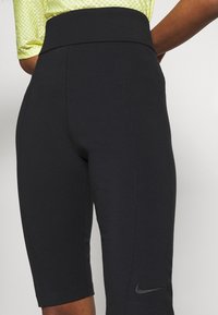 Shorts de sport noirs avec une taille haute, fabriqués en tissu extensible. Présente un logo Nike sur la jambe inférieure. Surface légèrement texturée.