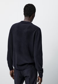 Pull en maille bleu marine avec un col rond côtelé, des manches longues et une coupe décontractée, doté d'une texture douce et d'un design subtil.