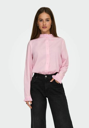 Chemise rose à manches longues avec un col et des poignets froncés, associée à un jean noir taille haute. Tissu lisse, coupe décontractée.