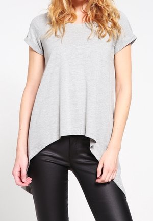 Woman wearing a loose, short-sleeve gray top with a high-low hem paired with tight black leather pants.