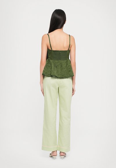 Green peplum top with textured fabric and adjustable straps, paired with light green wide-leg pants and pointed-toe heels.