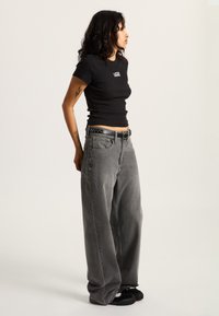 Black ribbed t-shirt with white "Vans" logo, paired with loose-fitting gray denim jeans and black shoes, featuring a textured belt.