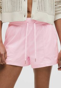 Pink shorts made of lightweight fabric with an elastic waistband and drawstring, featuring front pockets and a smooth texture.