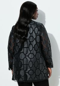 Schwarze Bluse zum Knöpfen mit strukturiertem, geometrischem Muster, durchscheinenden langen Ärmeln und lockerer Passform. Glattes, glänzendes Material.